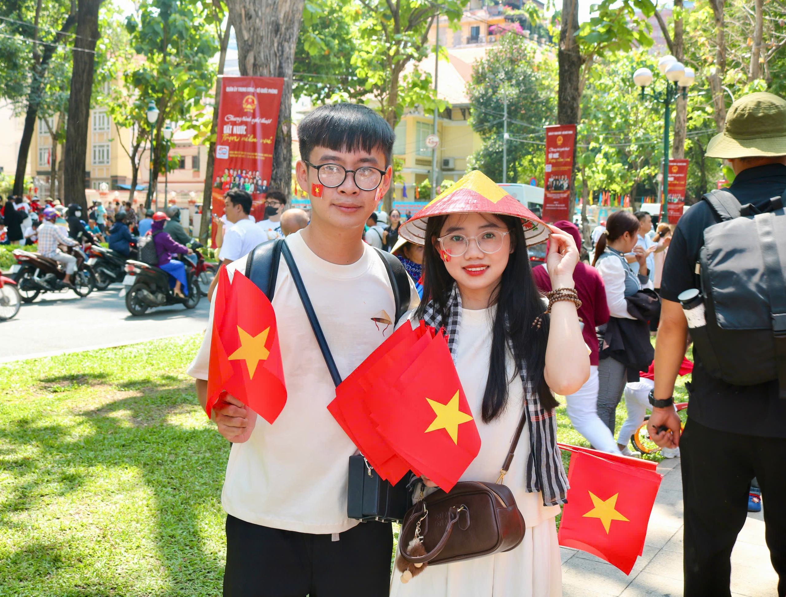 Hình ảnh đôi bạn trẻ đội nón lá, quấn khăn rằn, tay cầm cờ Tổ quốc