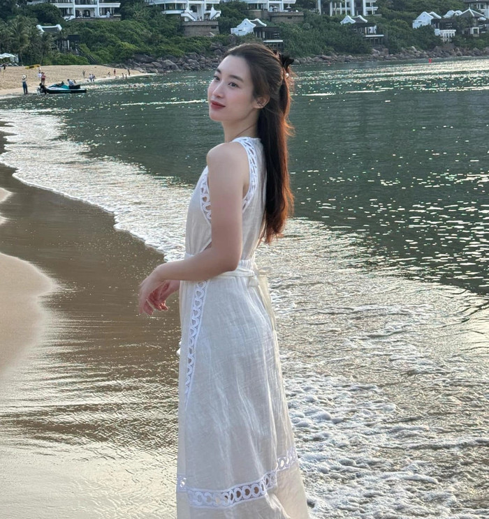 Một thiết kế khác trong tủ đồ của con dâu nhà bầu Hiển là đầm linen đắp ren tông beige nhạt. Chất linen thoáng mát, độ dài midi qua gối kết hợp chi tiết ren thủng tinh tế ở thân trước giúp Đỗ Mỹ Linh vừa sang trọng vừa phù hợp khí hậu biển. Điểm nhấn nằm ở đường may chiết nhẹ dưới ngực, tạo tỷ lệ thân trên ngắn, thân dưới dài, giúp vòng eo trông thon hơn dù không hề sử dụng corset hay kiểu váy bó sát. Ảnh: FBNV