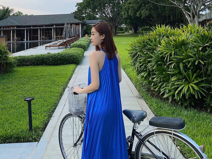 Đỗ Mỹ Linh trung thành với gu thời trang đi biển: váy maxi, đầm linen và lụa suông. Nổi bật nhất là chiếc váy maxi cổ yếm xanh bằng vải lụa mỏng nhẹ - item cô đã diện đi diện nhiều lần trong các kỳ nghỉ. Phom dáng suông rộng, dài qua mắt cá chân giúp che hoàn toàn phần bụng và đùi, nhưng phần cổ yếm halter lại khéo léo khoe xương quai xanh cùng bờ vai trần thanh thoát, tạo hiệu ứng thị giác thon gọn mà không cần lộ da thịt. Ảnh: FBNV